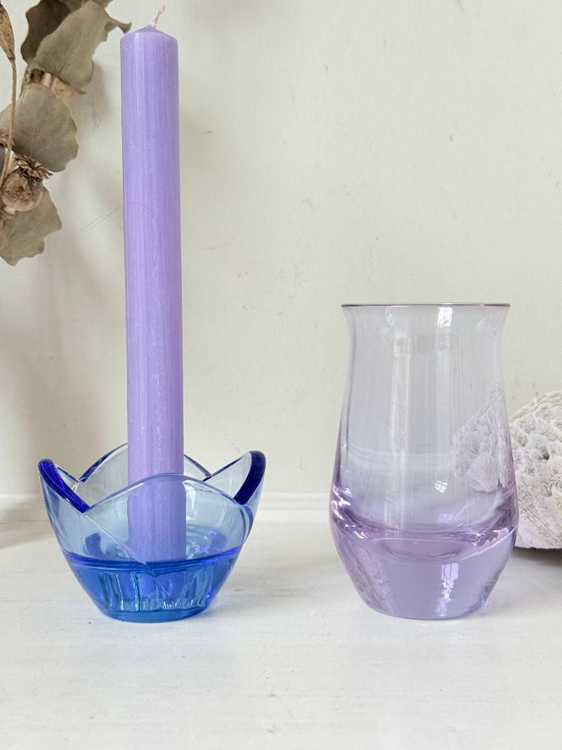 Blue Bormioli Rocco glass candlestick and lilac glass vase photographed on a white surface