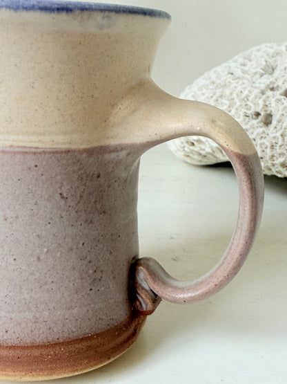 Studio pottery milk jug in cream and lavender glaze with impressed initials, photographed on a white surface.