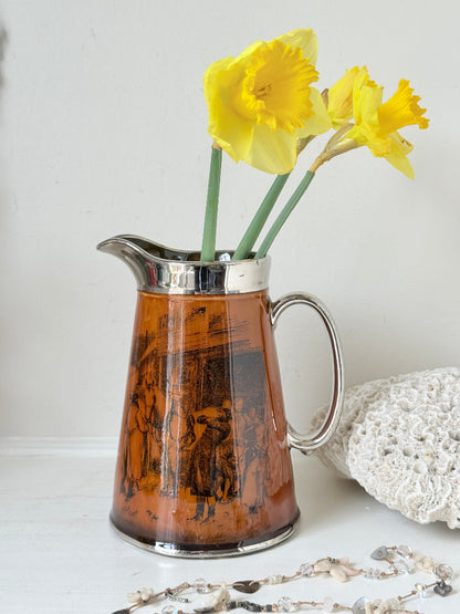 Antique Ridgways stoneware jug photographed on a white surface in amber treacle glaze with black Coaching Days and Coaching Ways scenes and silver lustre rim
