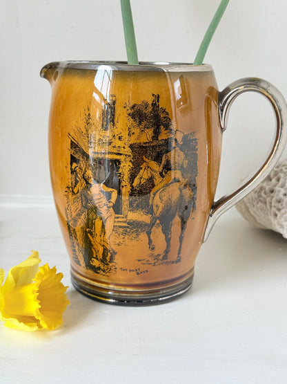 Antique Ridgways stoneware jug photographed on a white surface in amber treacle glaze with black Coaching Days and Coaching Ways transfer scenes and silver tone handle