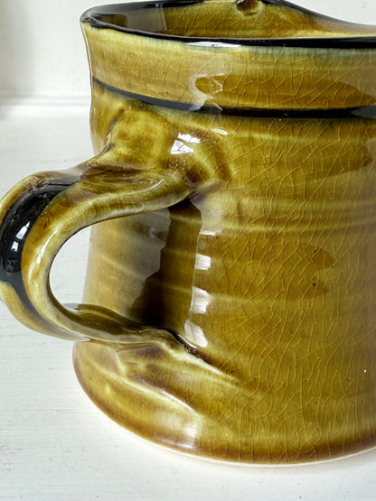 Studio pottery sugar bowl and milk jug in olive green glaze with black brushstroke decoration, photographed on a white surface.