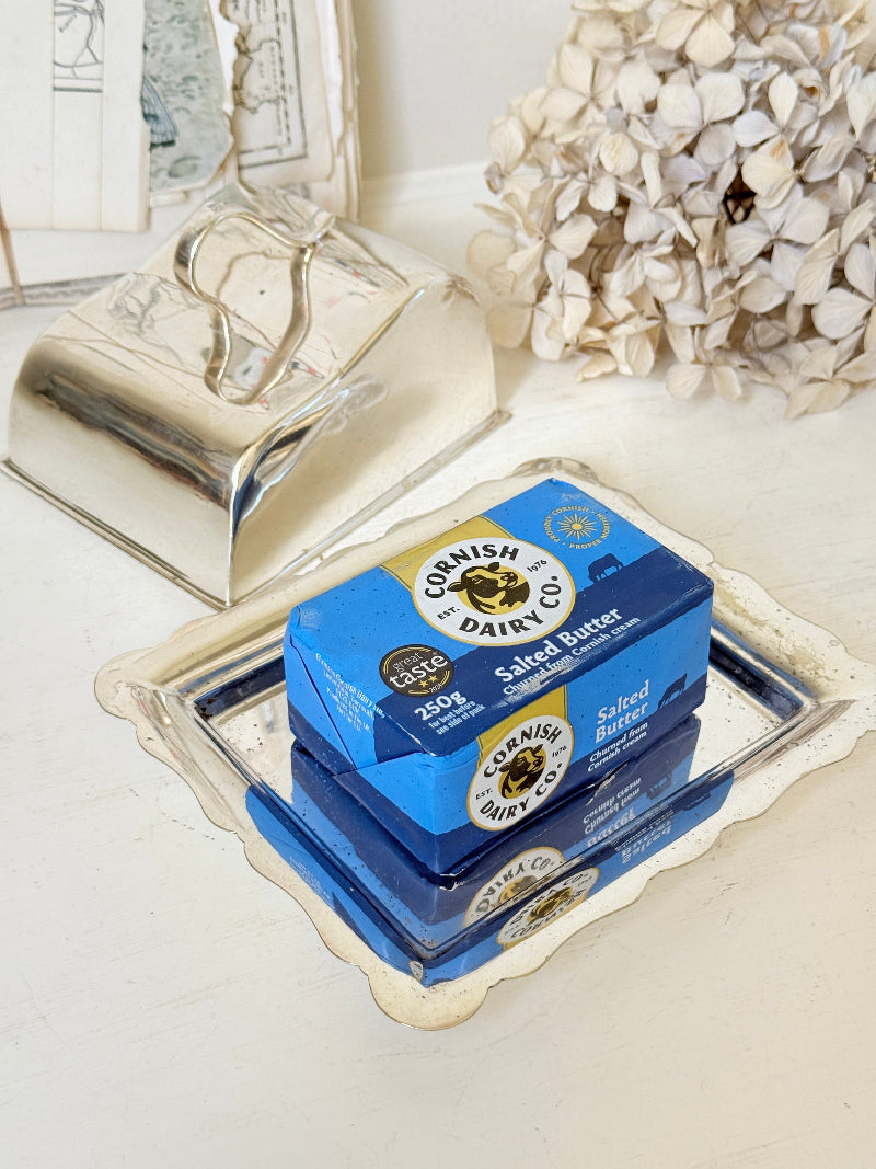 Two boxes of Cornish Dairy Co. Salted Butter stacked on a decorative silver tray, with a matching silver butter dish and dried flowers in the background.