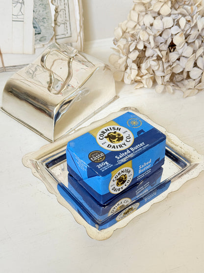 Two boxes of Cornish Dairy Co. Salted Butter stacked on a decorative silver tray, with a matching silver butter dish and dried flowers in the background.
