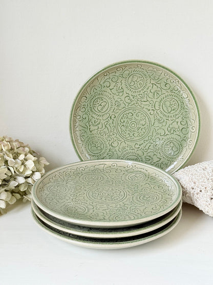 Set of four large Thai celadon stoneware plates in soft green glaze with raised pattern, photographed on a white surface
