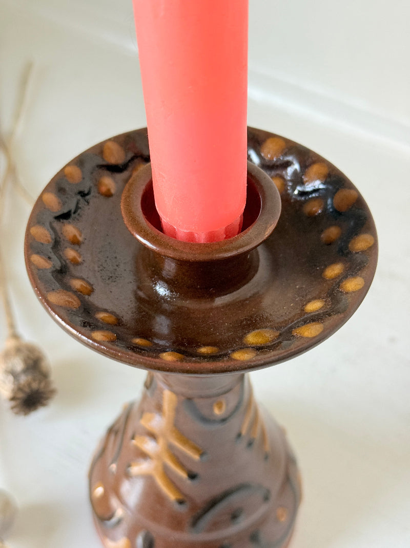 Vintage studio pottery candlestick in brown glaze with cut out decoration styled with coral taper candle on white surface