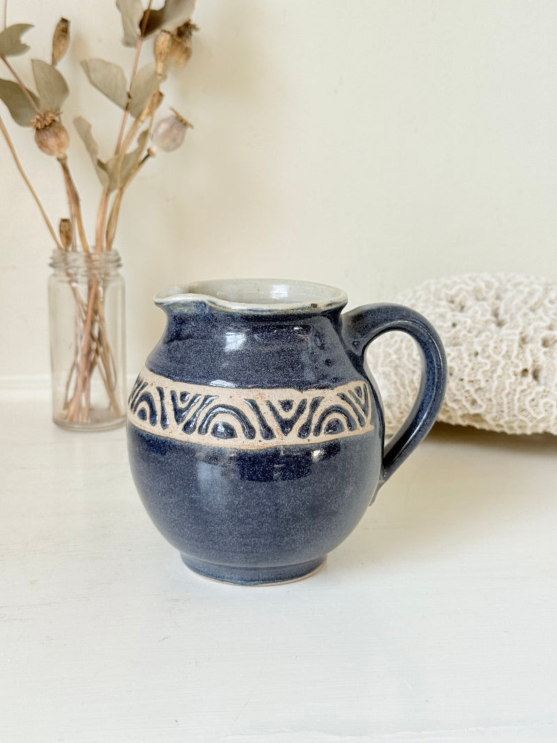 Studio pottery milk jug with deep blue glaze and cream geometric band, photographed on a white surface