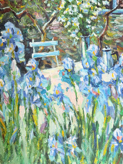 Framed impressionist-style oil painting of blue irises and garden scene, photographed on a white surface