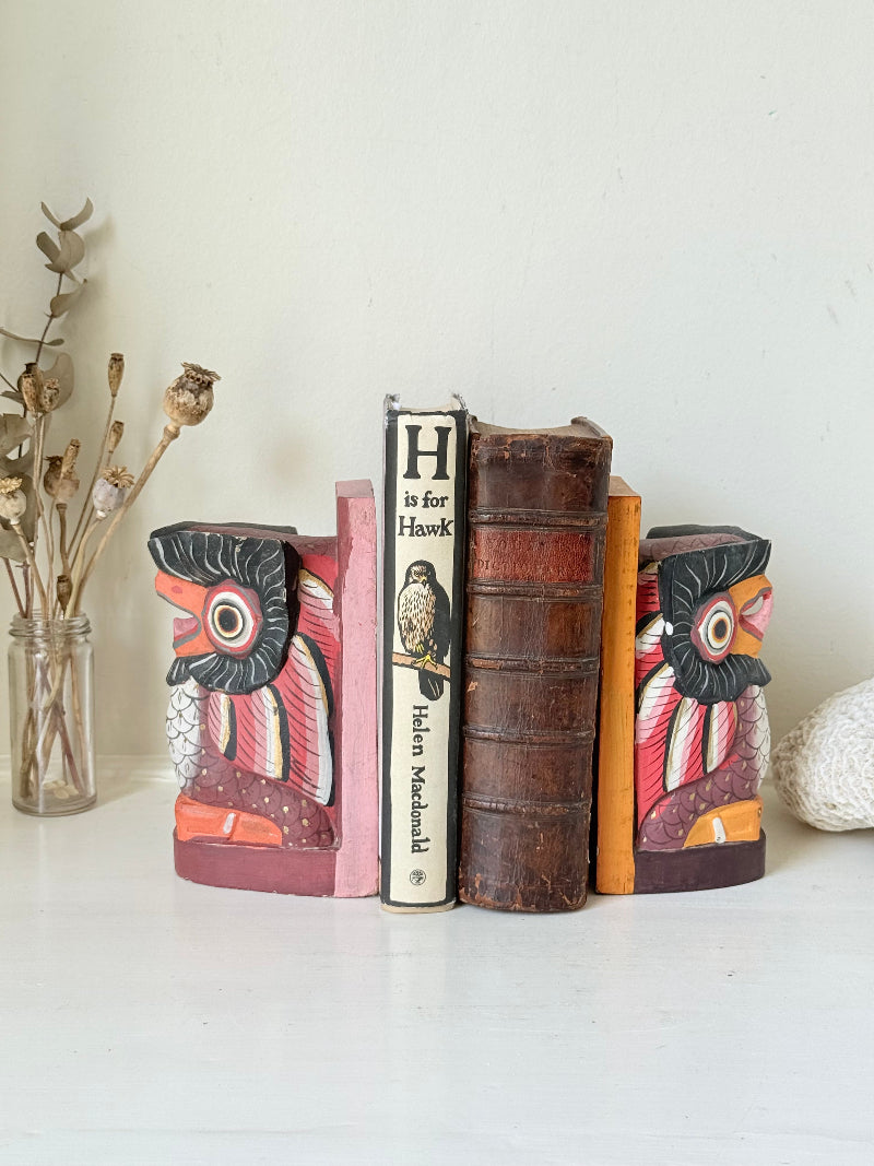 Vintage wooden owl bookends hand painted in red and orange tones, displayed on a white surface beside dried flowers.