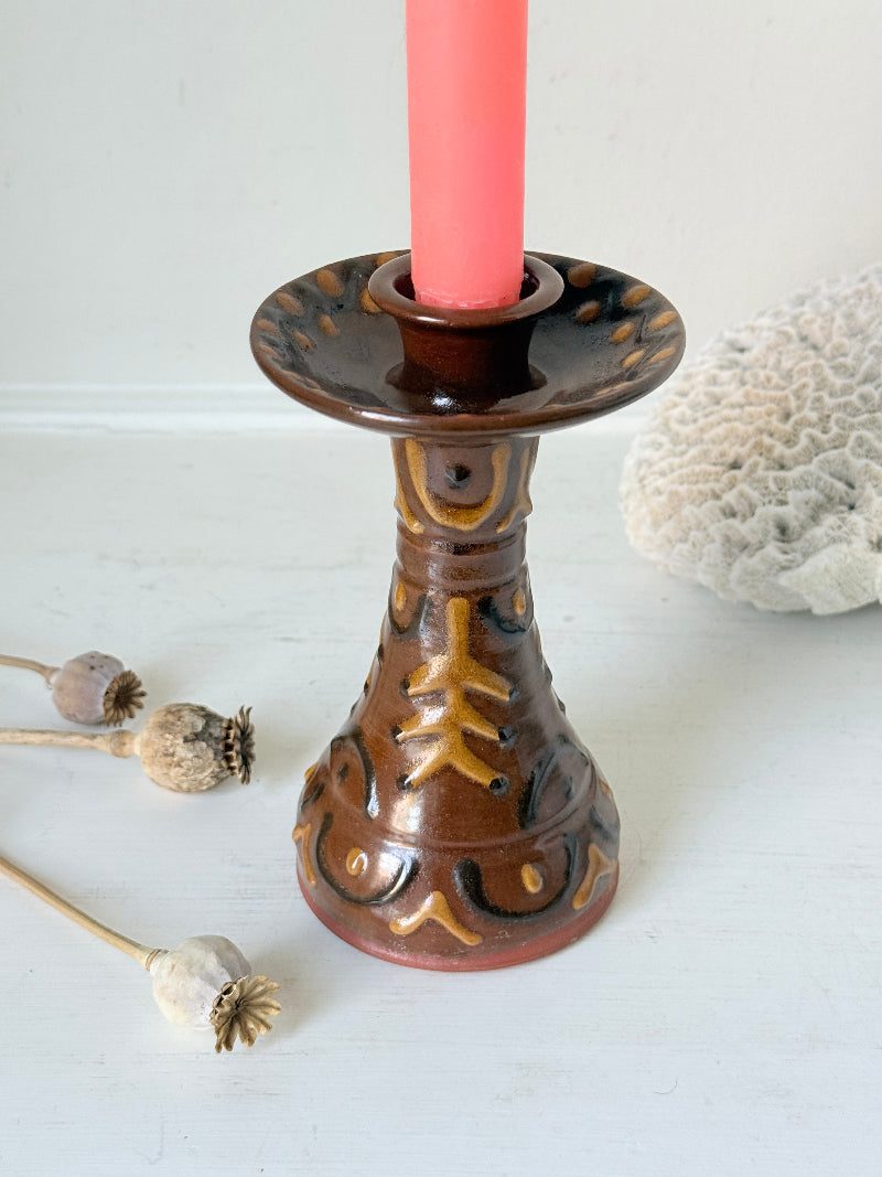 Vintage studio pottery candlestick in brown glaze with cut out decoration styled with coral taper candle on white surface