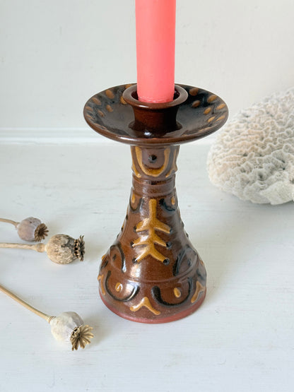 Vintage studio pottery candlestick in brown glaze with cut out decoration styled with coral taper candle on white surface