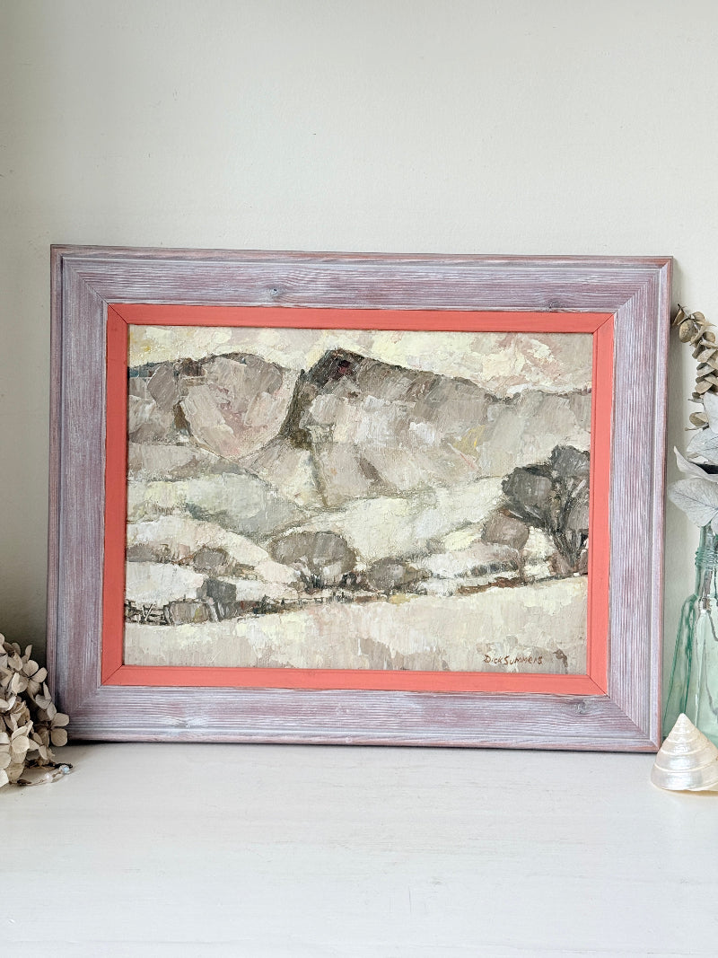 A framed landscape painting with a distressed lavender-gray wood frame and a coral-red mat, displayed on a white surface against a light gray wall.