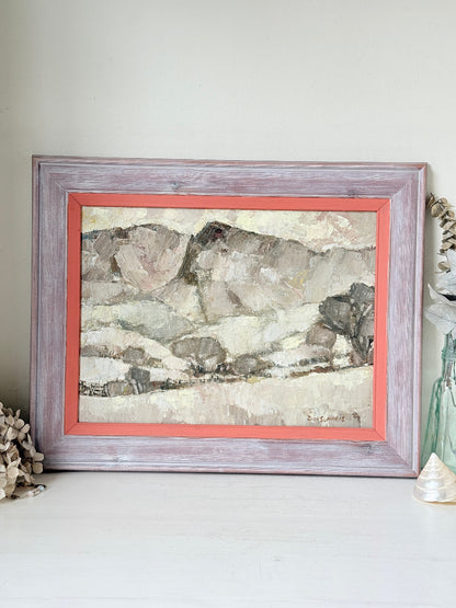 A framed landscape painting with a distressed lavender-gray wood frame and a coral-red mat, displayed on a white surface against a light gray wall.