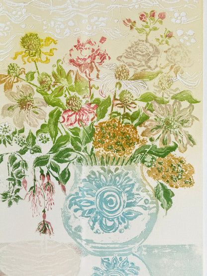 A vintage-style floral illustration featuring a bouquet of pink, yellow, white, and green flowers arranged in a light blue patterned vase against a cream background with subtle decorative borders.