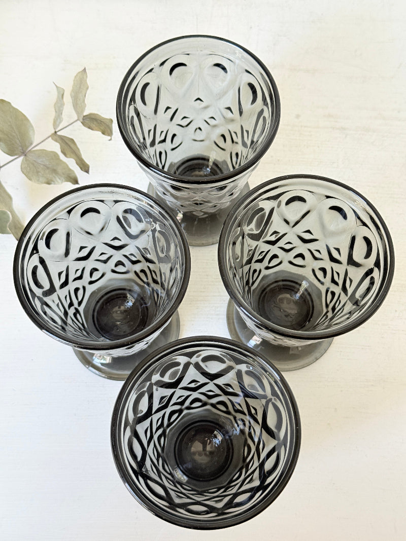 Set of four smoke grey pressed glass footed goblets with a diamond pattern, photographed on a white surface