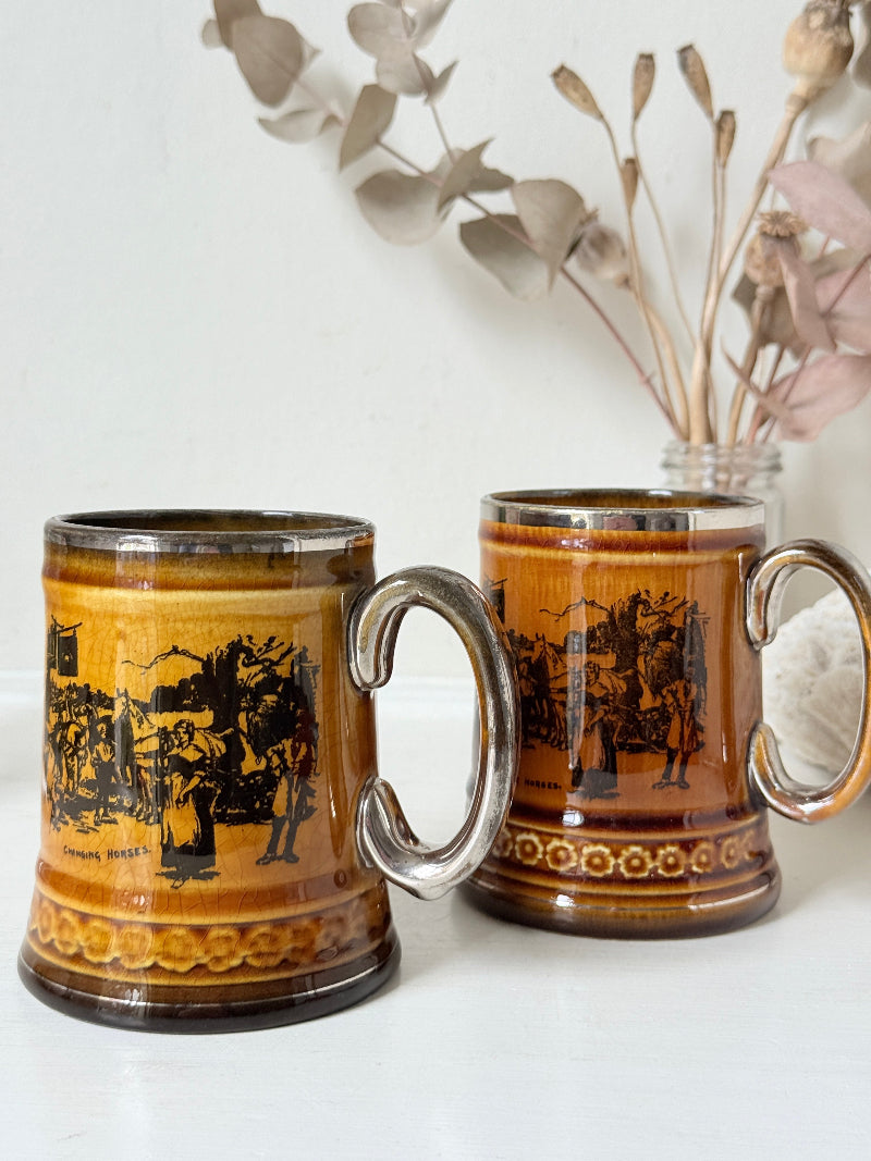 Pair of Ridgways stoneware tankard mugs photographed on a white surface in amber brown glaze with black Coaching Days and Coaching Ways transfer scenes