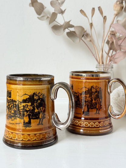 Pair of Ridgways stoneware tankard mugs photographed on a white surface in amber brown glaze with black Coaching Days and Coaching Ways transfer scenes
