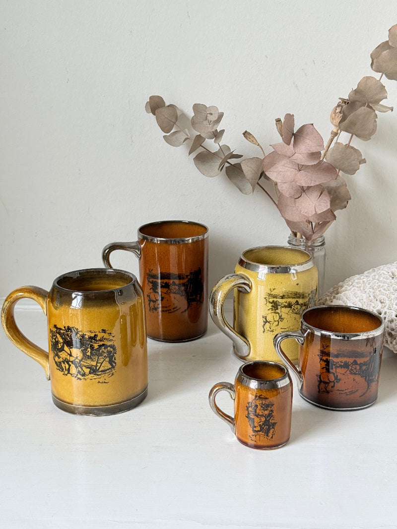 Set of 5 Ridgways stoneware mugs photographed on a white surface in amber brown glaze with black Coaching Days and Coaching Ways transfer scenes