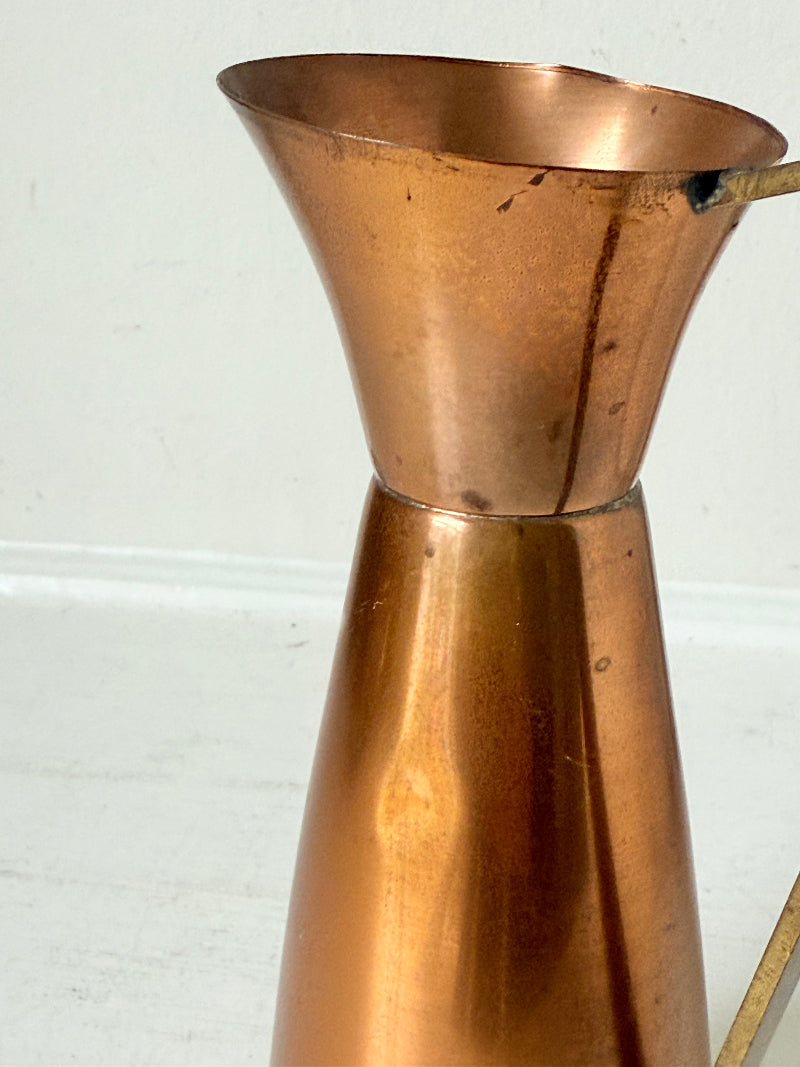 Vintage copper and brass jug with slender handle, photographed on a white surface