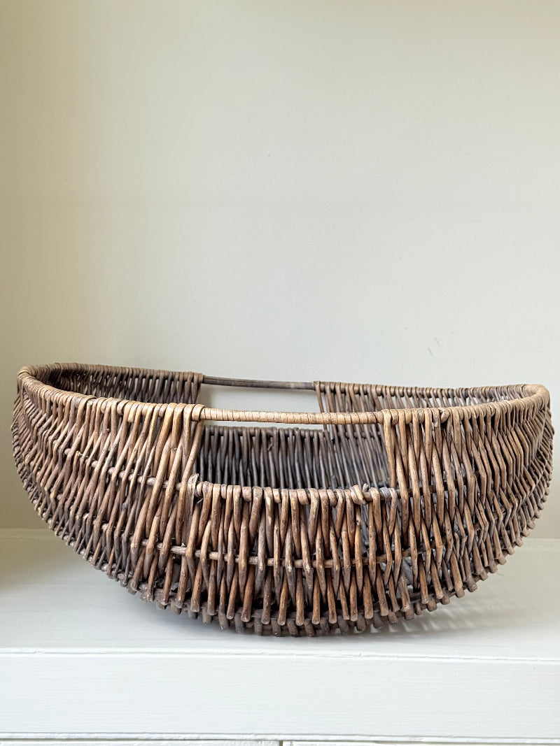 Large vintage woven basket with sculptural oval shape and integrated handles photographed on a white surface