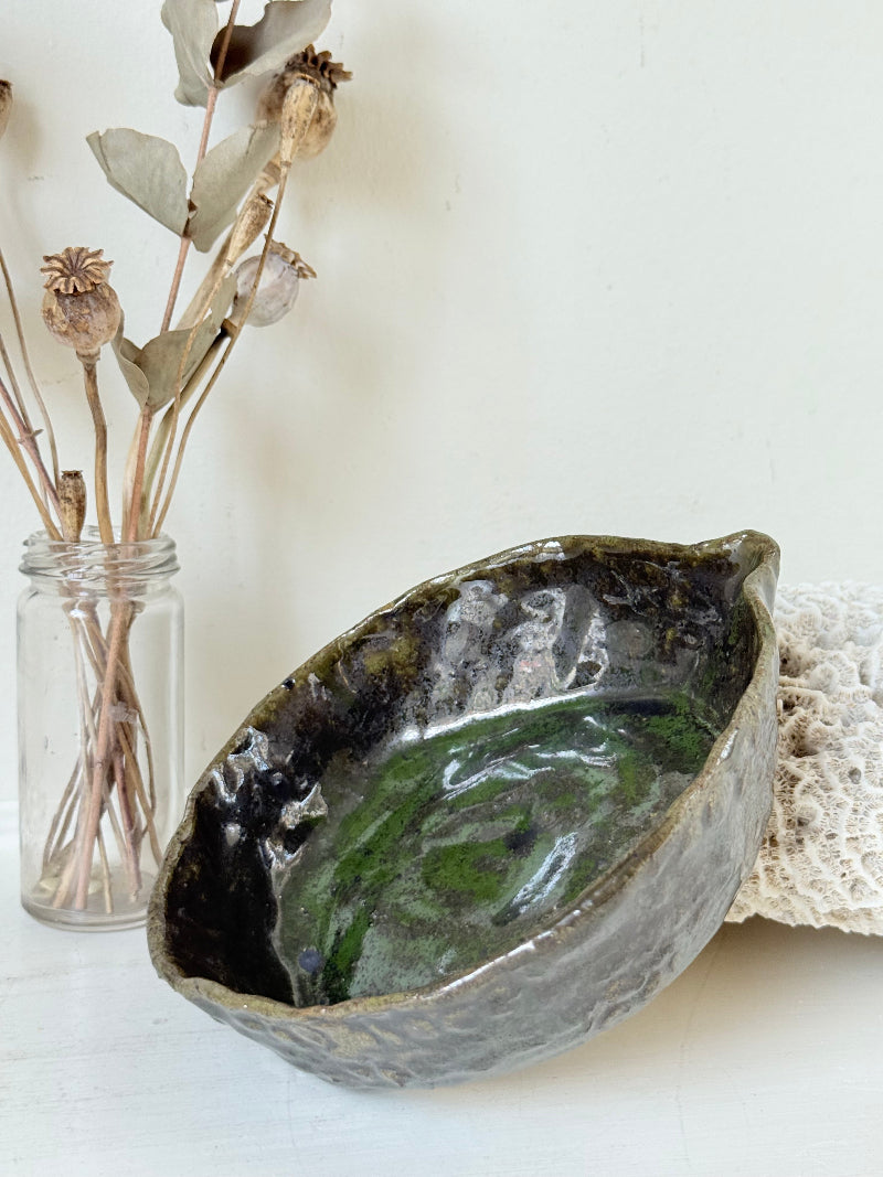 Studio pottery olive bowl with green and charcoal glaze, photographed on a white surface