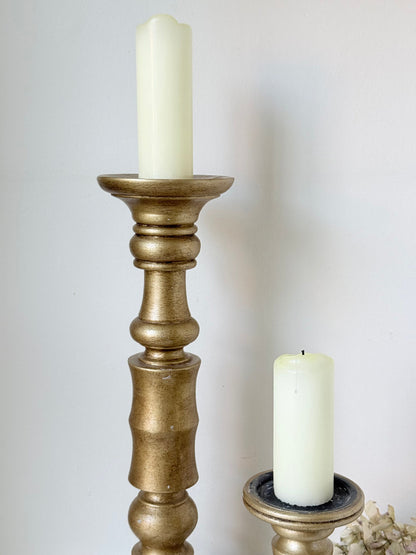 Pair of vintage wooden candlesticks, one tall and one small, in golden-toned finish, styled with pillar candles on a white surface.