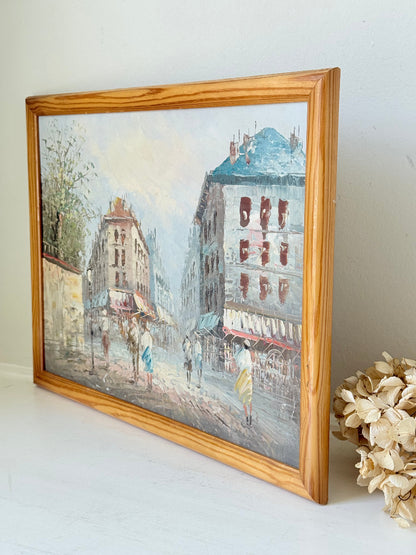 Vintage oil painting of European street scene with buildings and awnings in wooden frame photographed on a white surface

