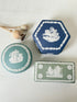 
Trio of vintage Wedgwood Jasperware lidded pots in Portland blue and sage green, featuring neoclassical white relief figures, styled with dried stems on a pale surface.