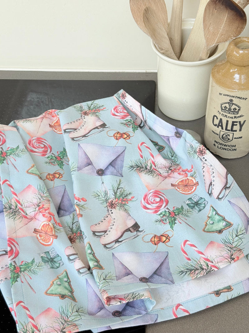 Blue Loft Christmas cotton tea towel with ice skate and candy pattern photographed on a white surface.