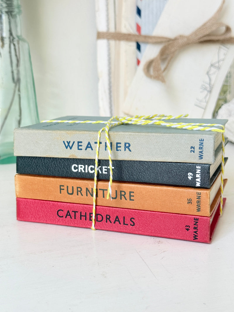 A stack of four textured book covers tied with yellow string, featuring the titles &