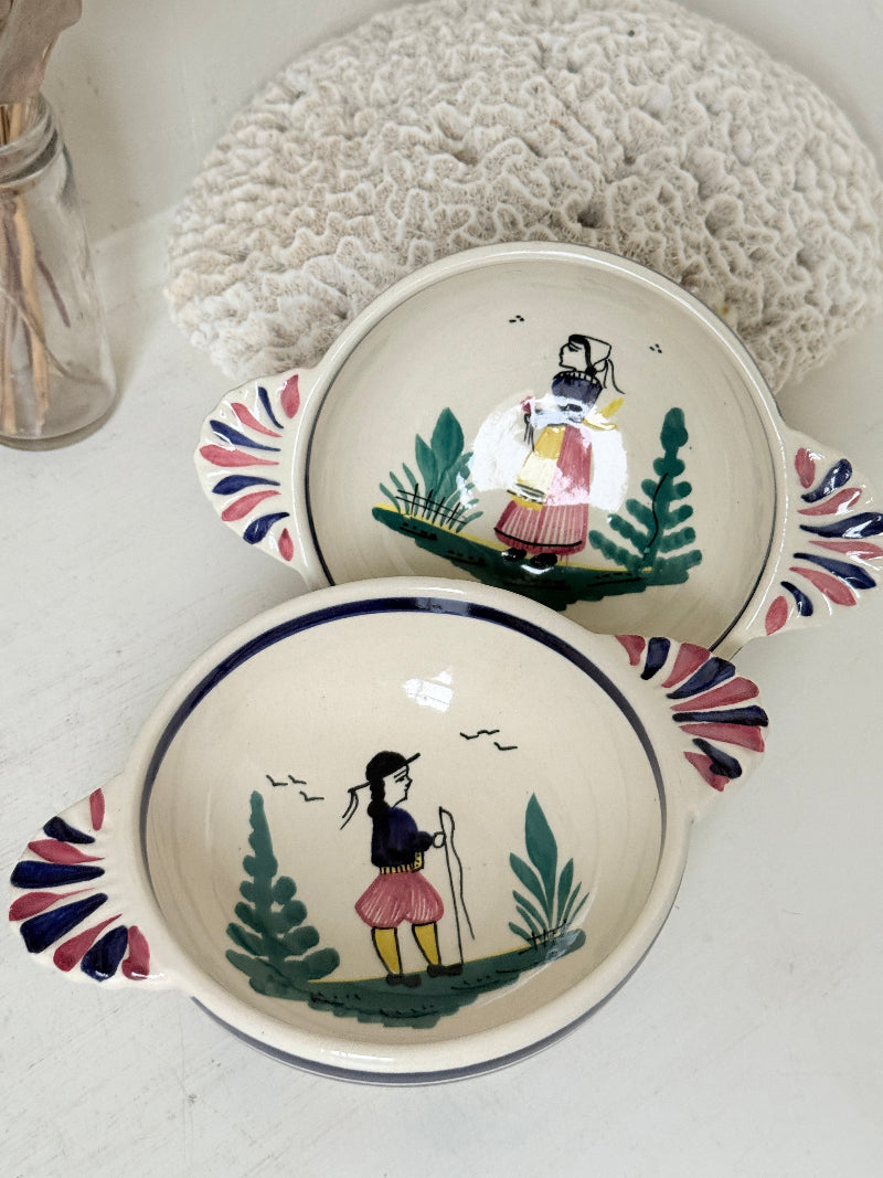 Pair of vintage French Quimper Breton figure snack bowls with painted side handles, photographed on a white surface