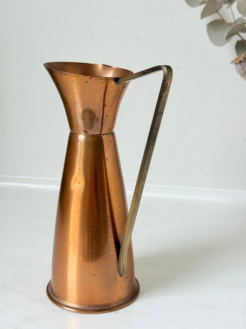 Vintage copper and brass jug with slender handle, photographed on a white surface
