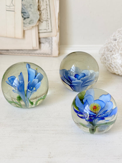 Trio of vintage glass paperweights with hand worked blue floral detail, clear glass domes and green leaf decoration