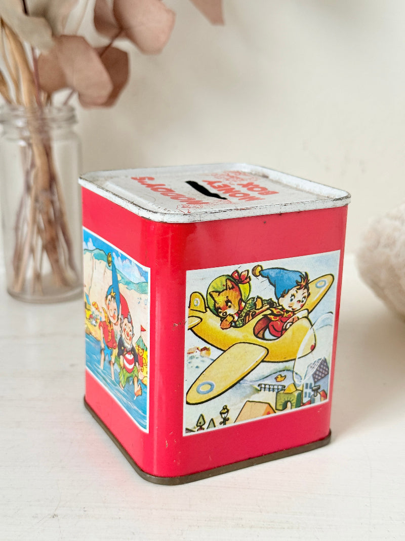 Vintage Noddy money box tin in red with illustrated panels, photographed on a white surface