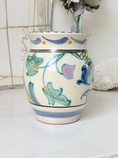Hand painted floral pottery vase in blue and green on cream, photographed on a white surface