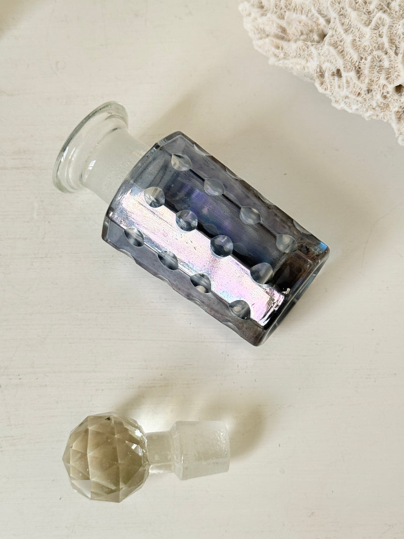 Vintage decagon iridescent glass perfume bottle with raised dot pattern and clear faceted stopper, photographed on a white surface