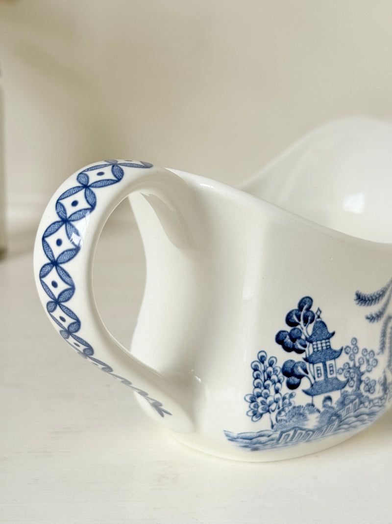 Vintage blue and white ceramic sauce boat with willow pattern photographed on a white surface