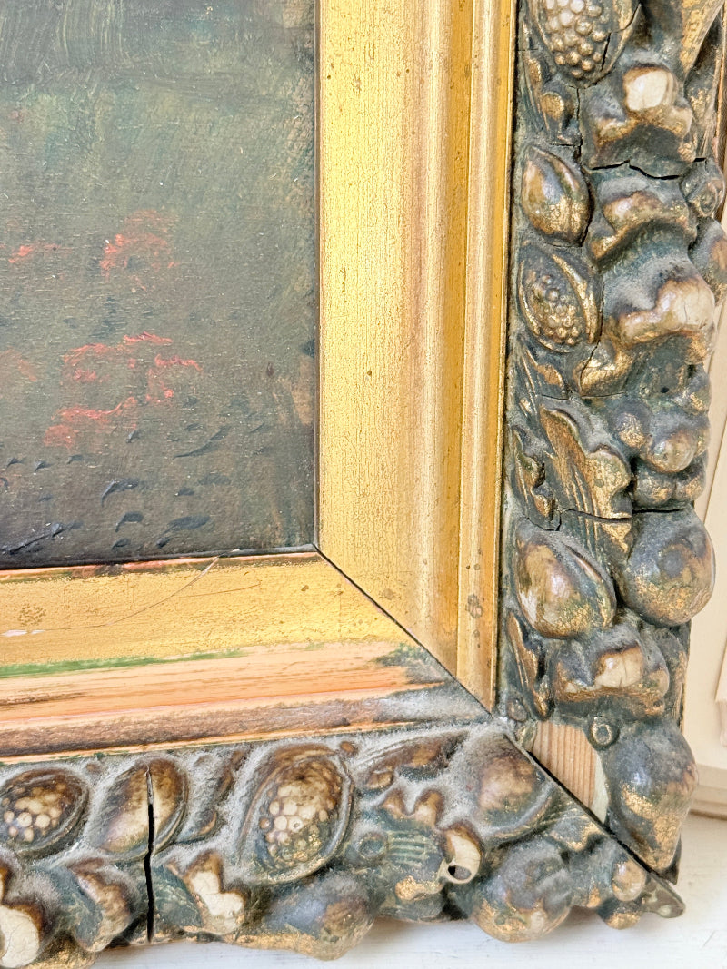Close-up of an ornate antique-style picture frame corner, showing a carved sculpted frame with a distressed gold inner border and a dark green-gray outer frame with raised organic textures.