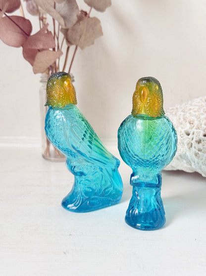 Pair of vintage Avon turquoise glass parrot bottles with green amber stoppers photographed on a white surface