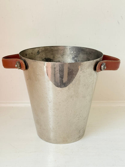 Vintage metal wine cooler with leather handles and tapered form, photographed on white surface.