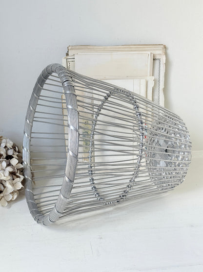 A silver metal wire basket-style wall decor piece with circular wire patterns, displayed against a white wall with a vintage-style frame behind it.