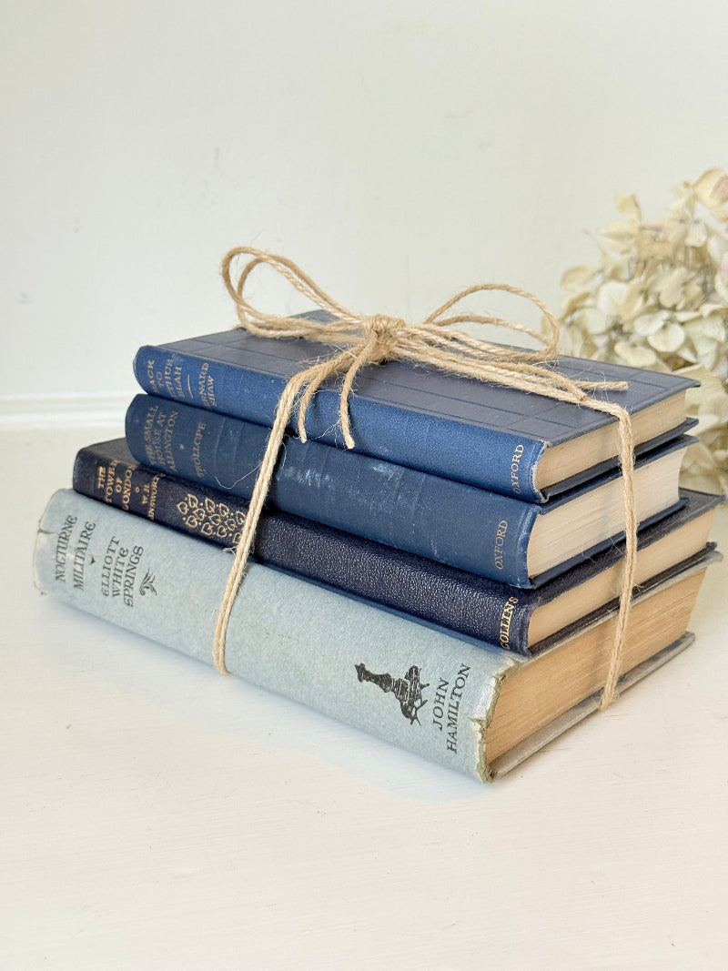 Vintage decorative book bundle in navy, grey, and cream tied with twine, photographed on a white surface
