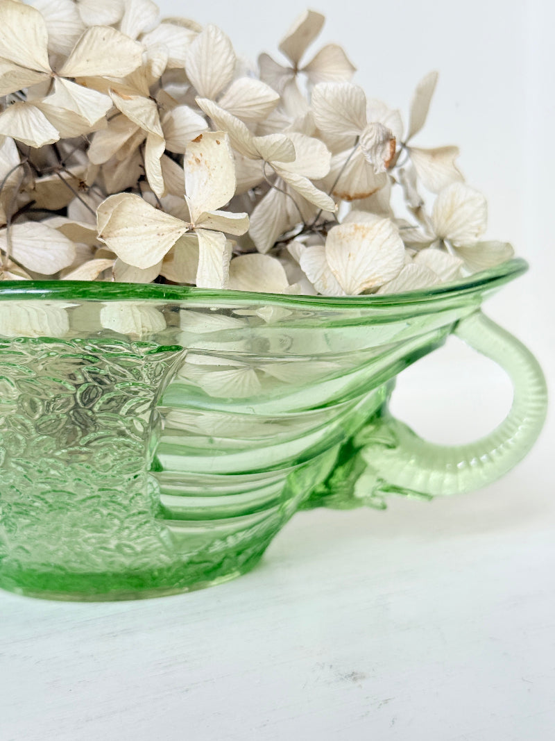 A green ribbed glass bowl filled with dried cream-colored flowers, set against a clean white background.