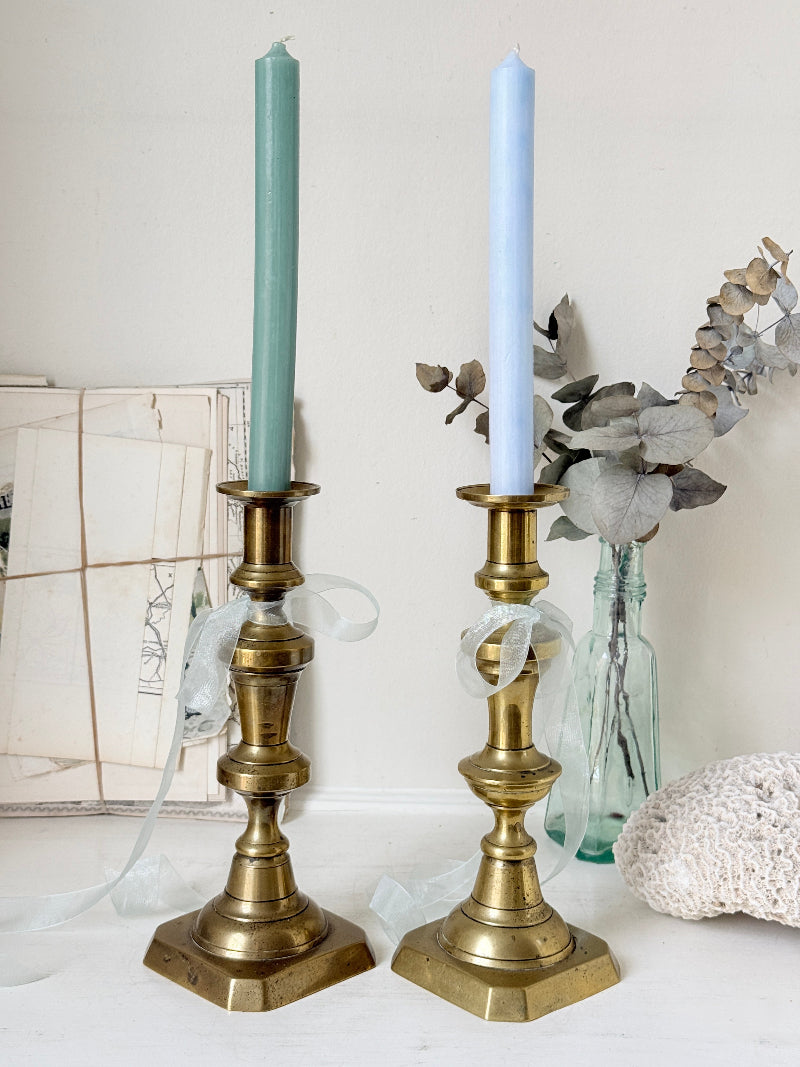 Pair of tall antique brass candlesticks with knopped columns and octagonal stepped bases holding blue and green tapers