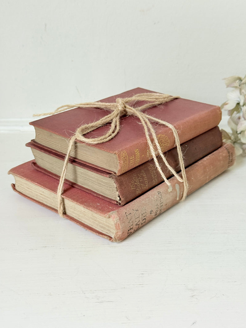 Bundle of three vintage books in worn rose and blush tones tied with natural twine, photographed on a white surface