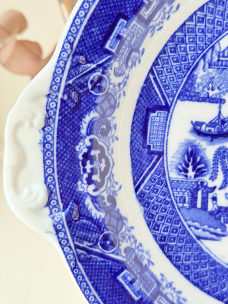 Blue Willow serving plate with scroll handled relief shown on a white surface.