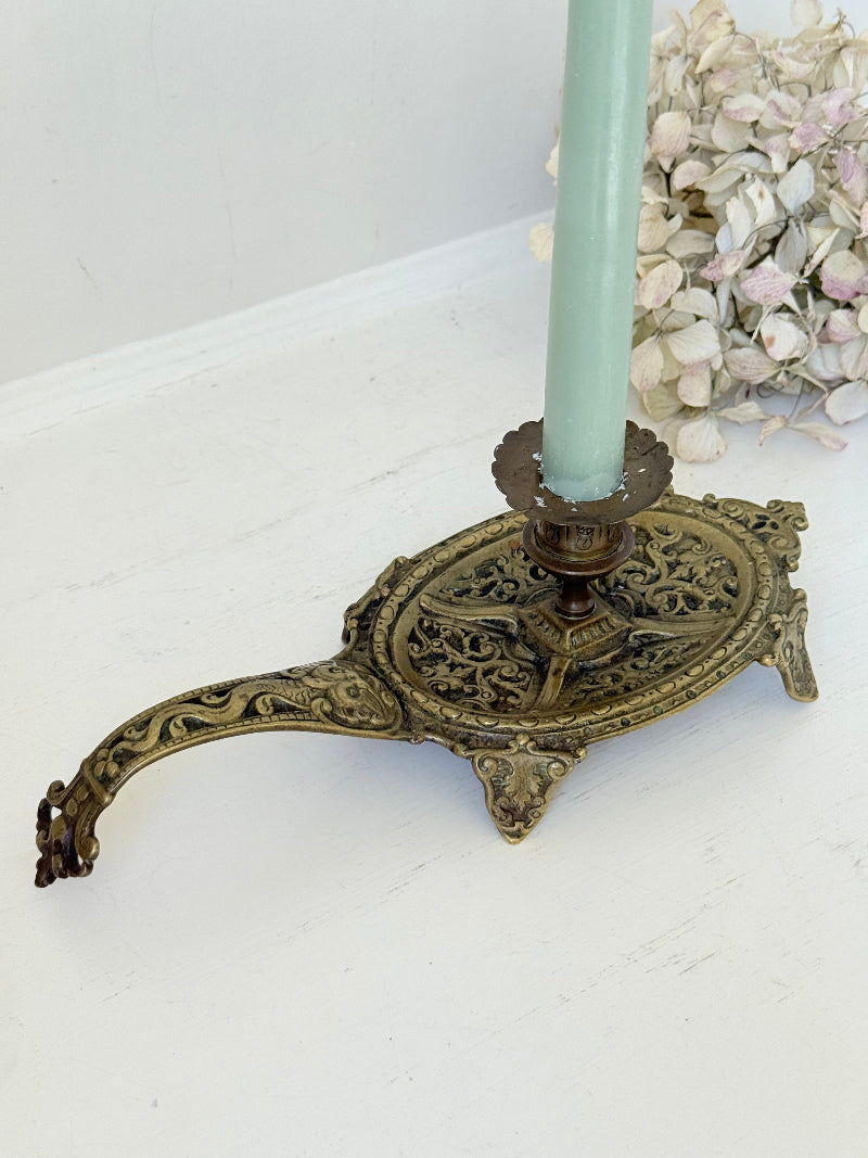 Ornate vintage brass candlestick with decorative handle and footed base, photographed on a white surface