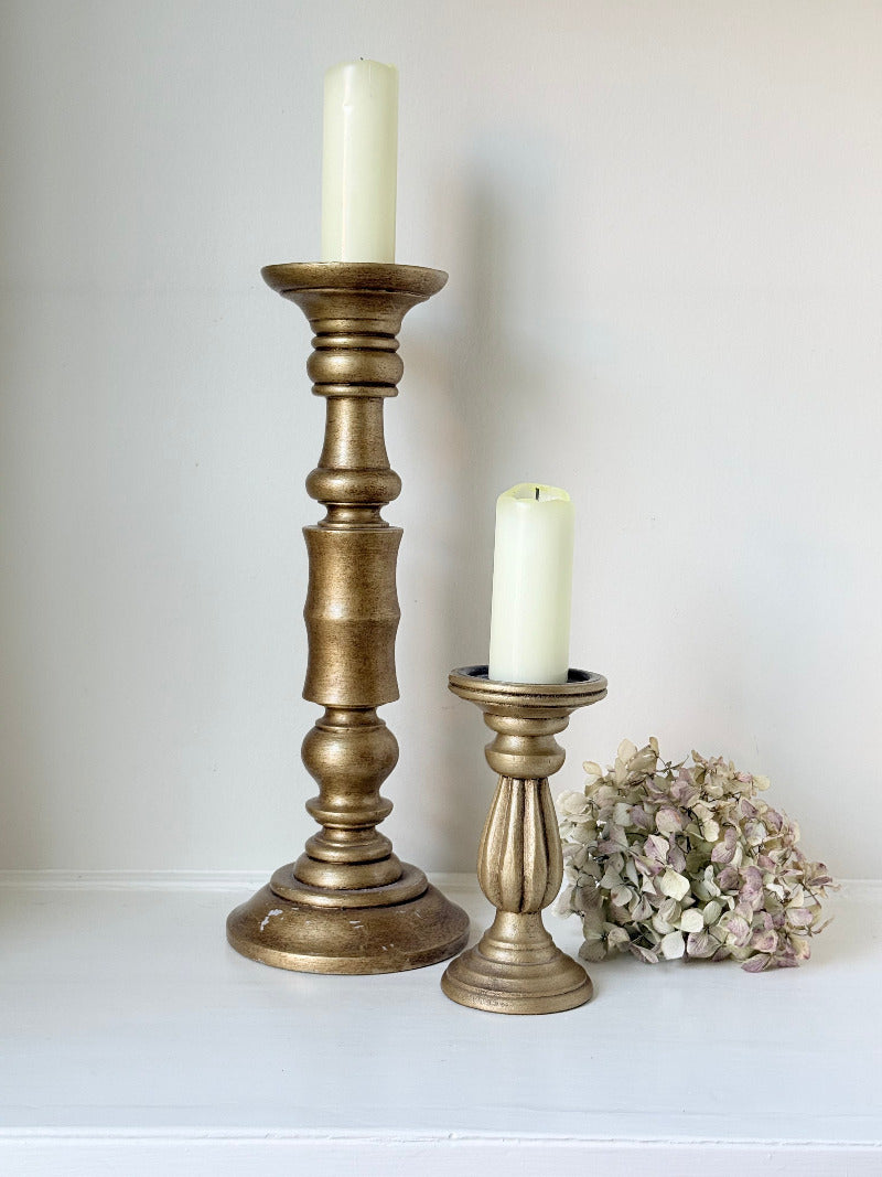 Pair of vintage wooden candlesticks, one tall and one small, in golden-toned finish, styled with pillar candles on a white surface.