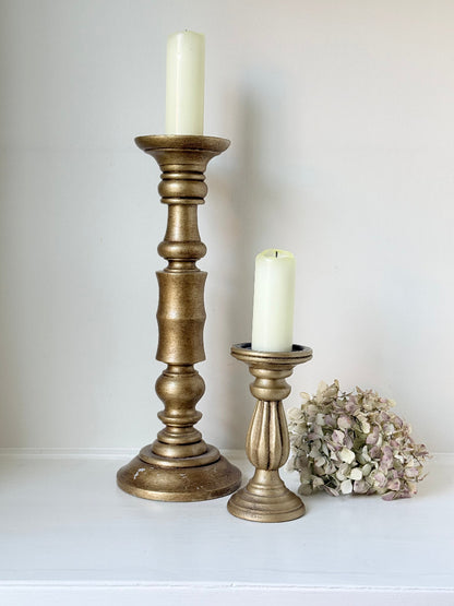 Pair of vintage wooden candlesticks, one tall and one small, in golden-toned finish, styled with pillar candles on a white surface.