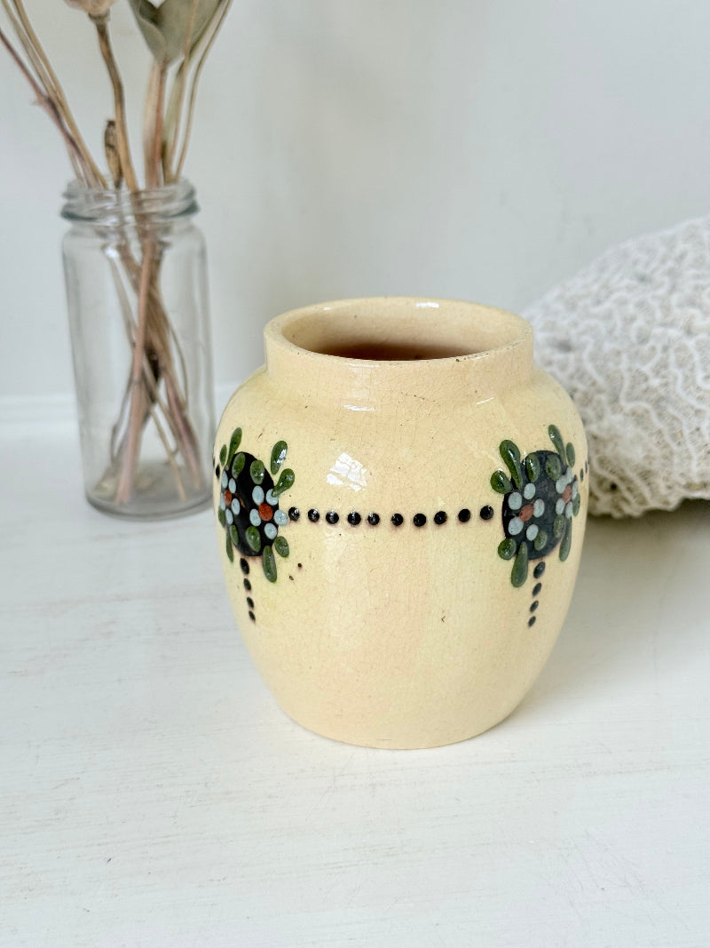 Cream studio pottery decorative pot with raised green floral motif, photographed on a white surface