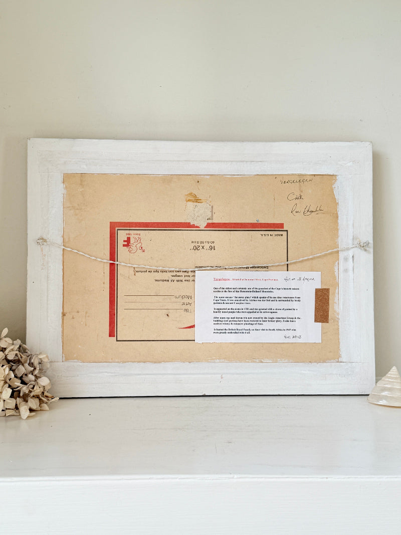 A square white wooden frame displayed on a white shelf, containing vintage paper documents and a red envelope, with a string across the front and dried flowers at the side.
